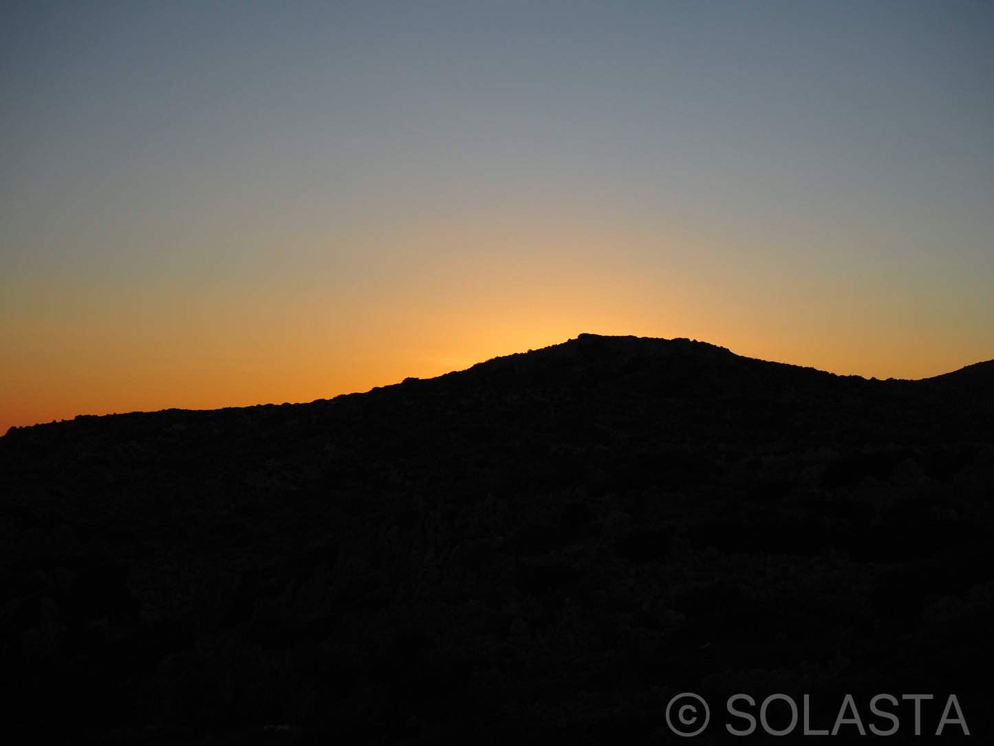 Mountain silhouette against vivid sunset sky with orange and yellow gradient