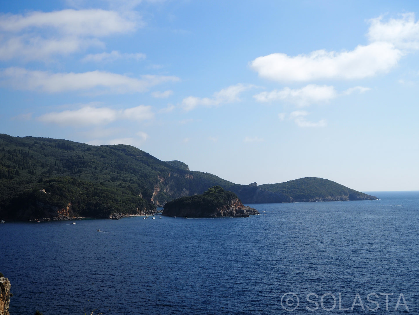 Two rocky islands in deep blue water with scattered clouds and green vegetation on surrounding slopes