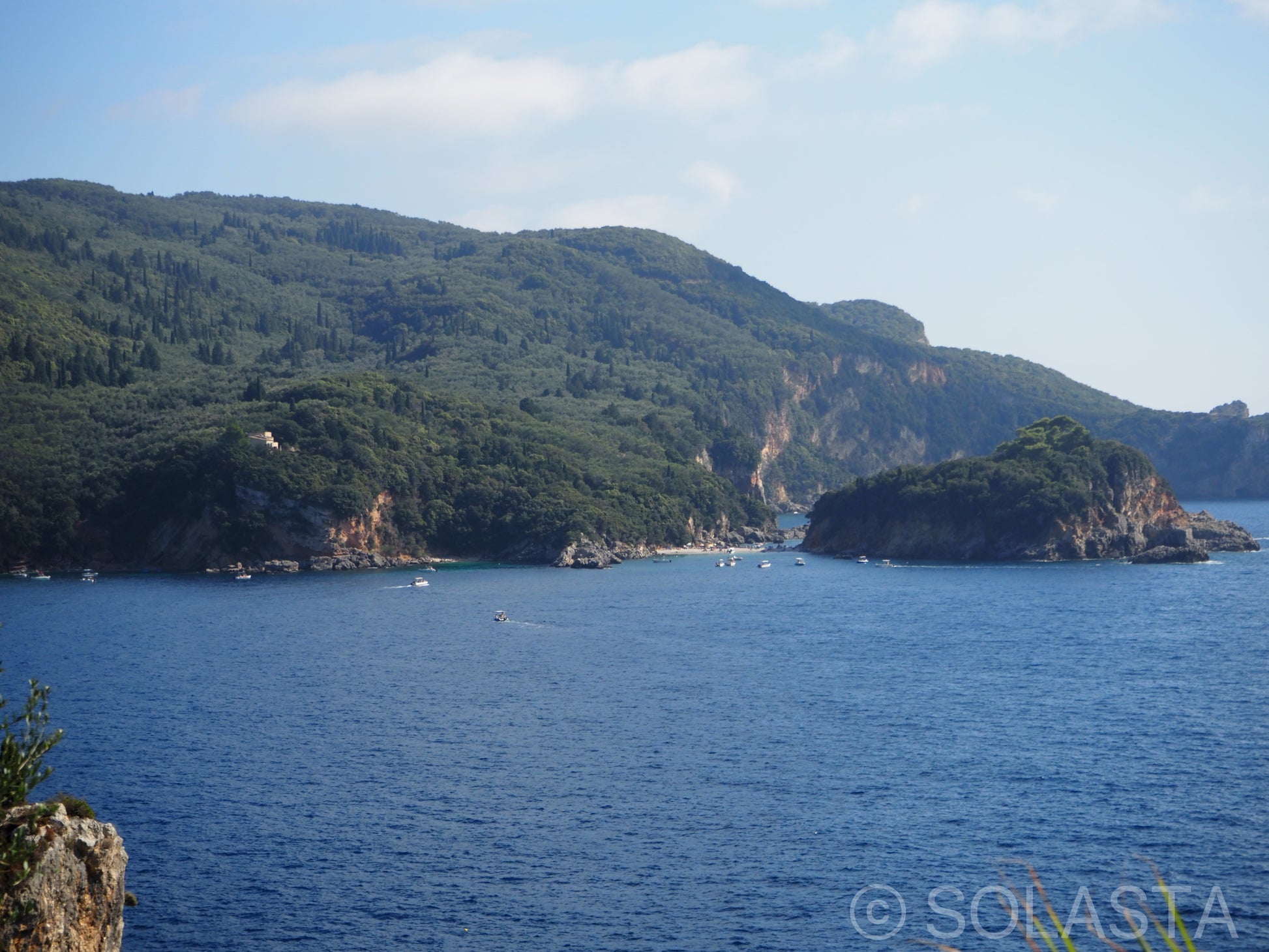 Calm bay with scattered green islands reflected in still blue water under clear sky