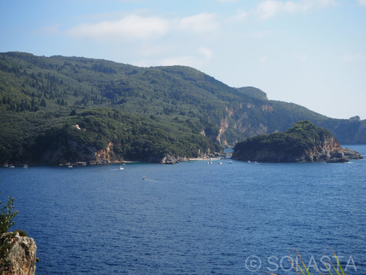 Calm bay with scattered green islands reflected in still blue water under clear sky