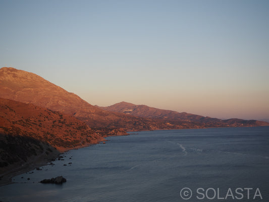 Aerial view of coastal mountains at sunset with orange and pink sky reflecting over the ocean